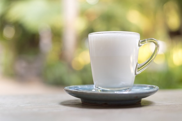 Leche blanca y caliente en un vaso colocado sobre una mesa con un fondo verde