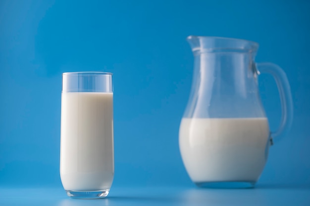 Leche blanca en una jarra y vaso sobre un fondo azul, cerrar