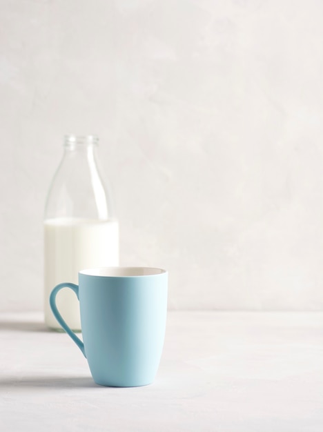 La leche en una botella de vidrio con una taza azul se encuentra sobre una mesa de hormigón gris.