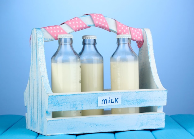 Leche en botellas en caja de madera sobre mesa de madera azul sobre fondo azul.