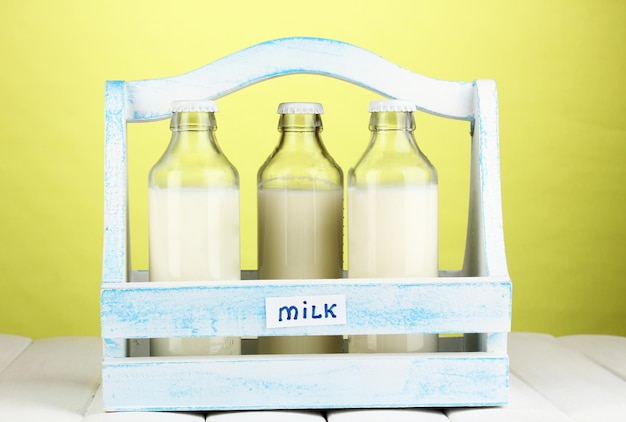 Leche en botellas en caja de madera sobre mesa de madera sobre fondo verde