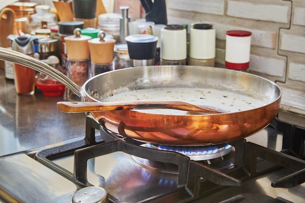 La leche y las cebollas picadas se fríen en una sartén de cobre sobre un fuego de gas