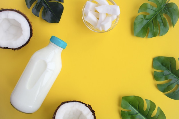 Leche de coco en la botella de vidrio sobre el fondo amarillo. Vista superior. Copie el espacio.