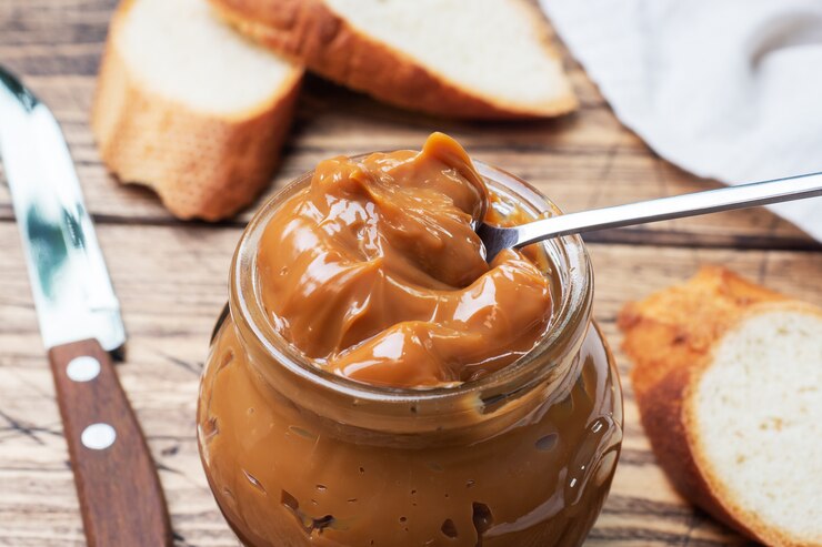 Leche condensada hervida con un frasco de vidrio sobre una mesa de madera. Pasta dulce untada en rebanadas de pan para el desayuno y el postre.