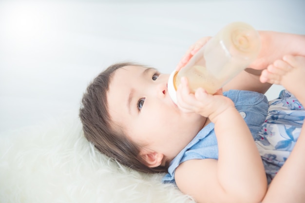 Leche de consumo del pequeño bebé asiático de la botella sola en cama