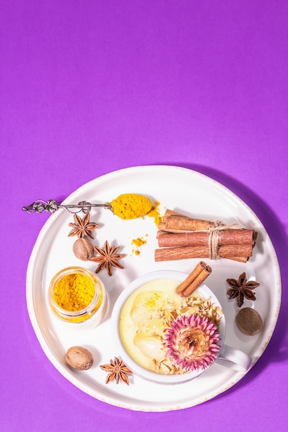 Leche de cúrcuma dorada con hielo. Especias de canela, nuez moscada, anís. Concepto de bebida de desayuno saludable por la mañana. Una luz dura moderna, sombra oscura, fondo lila pastel, vista superior