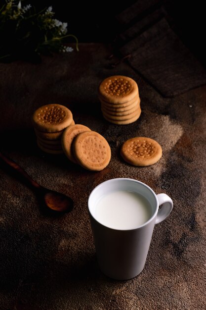 Leche fresca con galletas caseras en una mesa de madera, fondo oscuro.