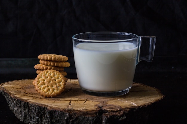 Leche fresca y saludable en taza y pila de galletas sobre fondo negro