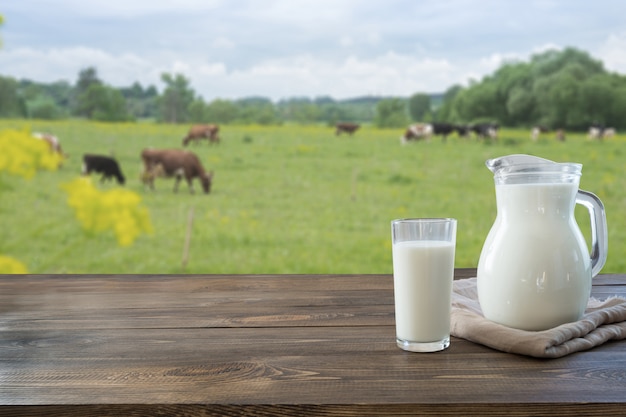 Leche fresca en vidrio en la mesa de madera oscura y paisaje borroso con vaca en Prado. Alimentación saludable. Estilo rústico