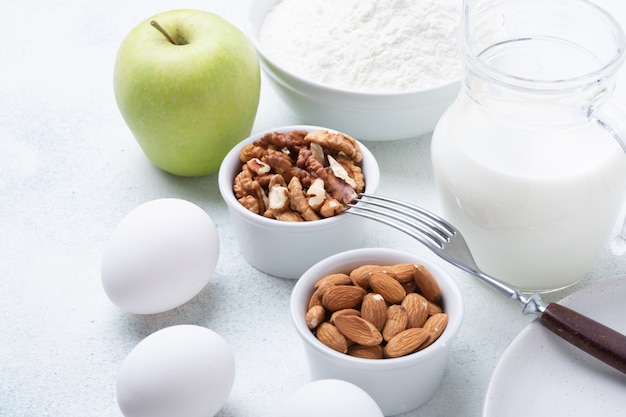 Foto leche, harina, huevos, nueces y manzanas verdes en una mesa de madera. ingredientes para la manzana charlotte. receta