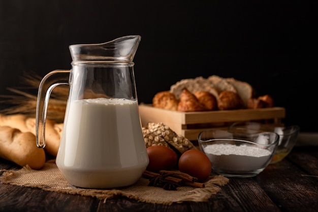 Leche en una jarra colocada sobre una mesa de madera con ingredientes.