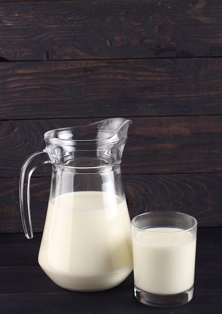 Foto leche en una jarra y un vaso sobre tablas oscuras