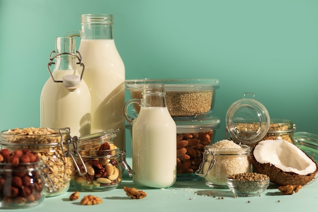 Leche láctea sustituto vegano. Botellas de vidrio con leche e ingredientes no lácteos sobre fondo azul con espacio de copia.