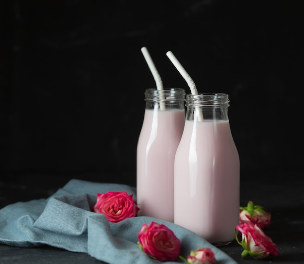 Leche de luna preparada con flor rosa rosa en dos botellas sobre un fondo negro