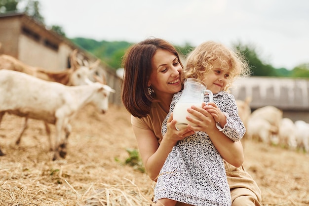 Leche natural fresca La joven madre con su hija está en la granja en verano con cabras