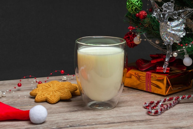 Leche navideña y pan de jengibre para Santa. Un vaso grande con leche y adornos navideños. Foto de una bebida navideña sobre un fondo de madera. De cerca