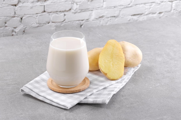 Leche de patata vegana en un vaso y tubérculos de patata sobre fondo de mesa de piedra gris a base de plantas