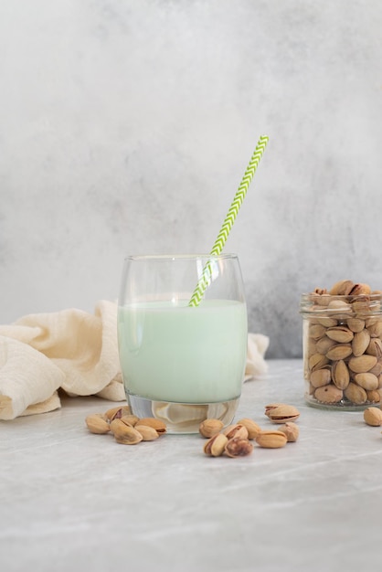 Leche de pistacho en un vaso con paja y pistachos sobre un fondo gris