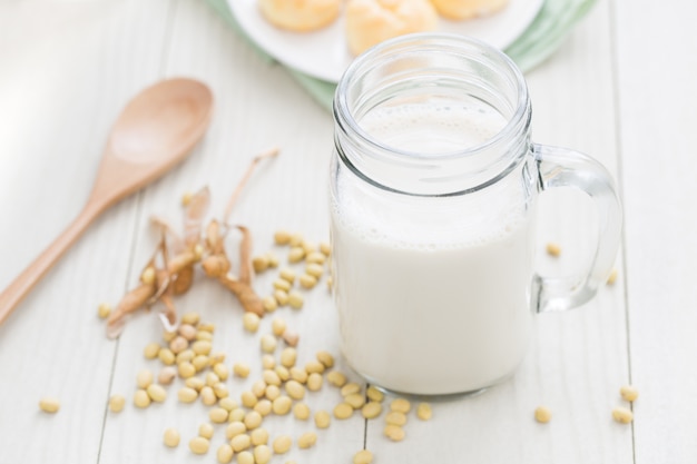 Leche de soja en un vaso, soja en una mesa blanca