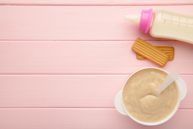 Leche y tazón con papilla para bebé en superficie rosa