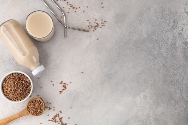 Leche de trigo sarraceno en una botella y un vaso de vidrio con un ingrediente sobre un fondo claro