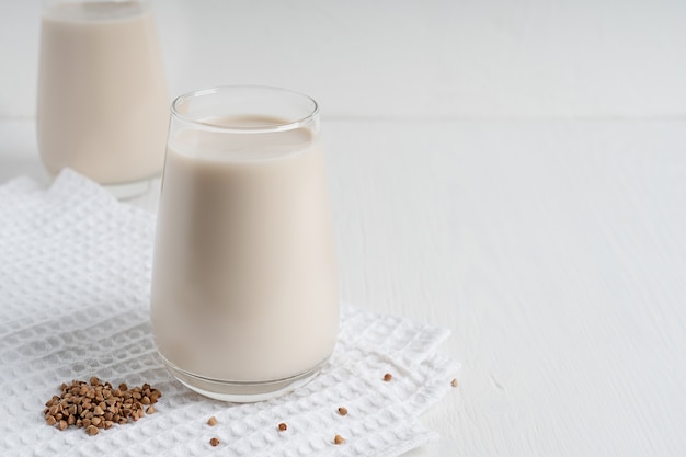 Leche de trigo sarraceno vegetariana sin lactosa servida en vaso sobre textil en mesa de madera blanca