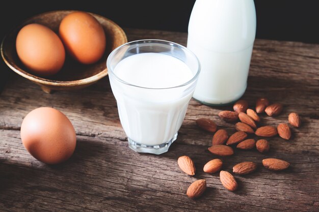 Leche en vaso y botella con huevos y almendras en la mesa de madera