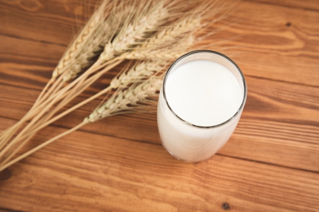 Leche en un vaso y trigo en una mesa de madera