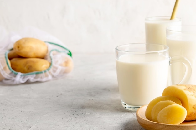 Leche vegetal de patata vegana en vasos y tubérculos de patata sobre fondo de hormigón con espacio de copia