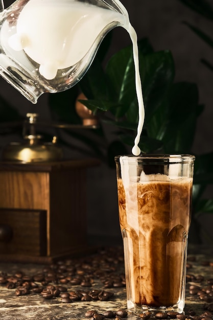 La leche se vierte en el café para hacer café con leche o café helado en un vaso Enfoque selectivo de tiro vertical