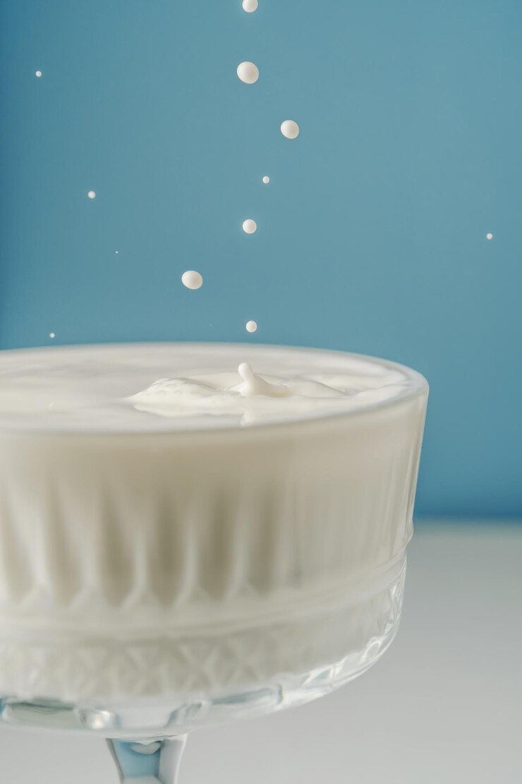 Foto la leche se vierte en un hermoso vaso de cristal sobre un fondo azul y salpica alrededor