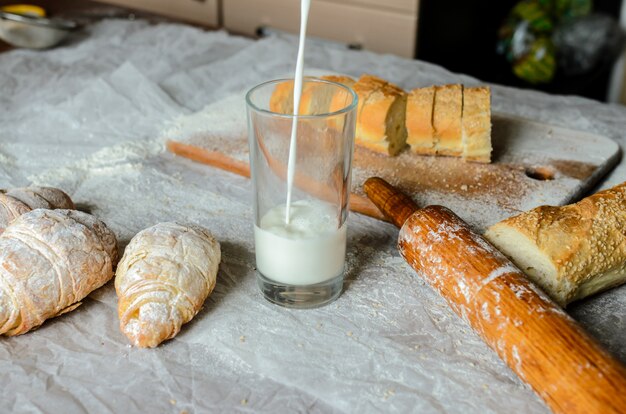 La leche se vierte en un vaso, pan, croissants.