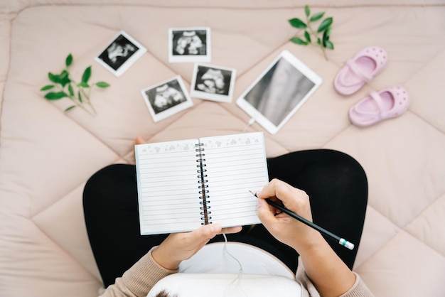 Una lechería de embarazoVista superior de una mujer embarazada escribiendo pensamientos en un cuaderno para la memoriaImagen de rayos x de su bebé y zapatosConcepto de embarazo Atención prenatal de maternidad