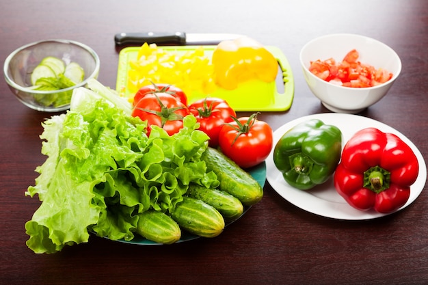 Lechuga con pepinos, tomates, pimientos, tabla de cortar y cuchillo sobre la mesa.