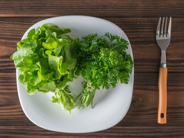 Lechuga y perejil en un recipiente blanco sobre una mesa de madera con un tenedor. El concepto de alimentación saludable. Endecha plana.