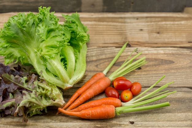 La lechuga, la zanahoria y el tomate frescos en el viejo fondo de madera