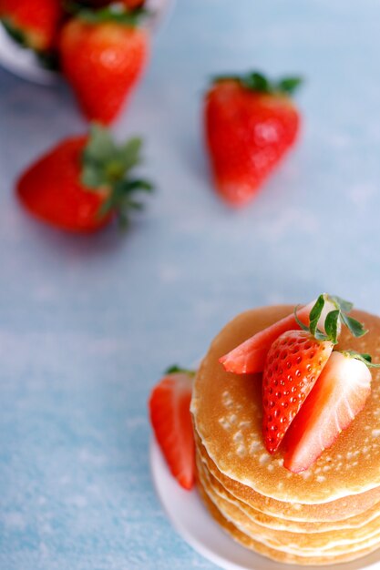 Leckere amerikanische Pfannkuchen mit Erdbeeren auf weißem Teller gegen blauen Hintergrund