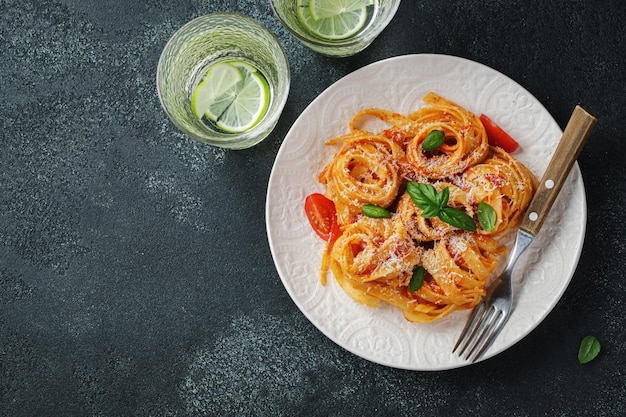 Leckere, appetitanregende klassische italienische Tagliatelle-Nudeln mit Tomatensauce, Käse, Parmesan und Basilikum auf dem Teller auf dunklem Tisch Ansicht von oben horizontal Draufsicht mit Kopierbereich