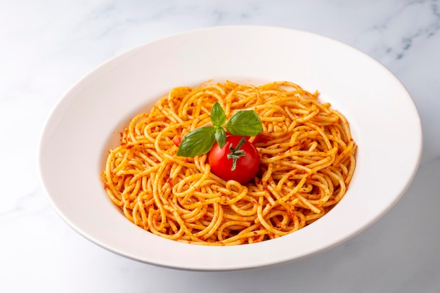 Leckere appetitliche klassische italienische Spaghetti-Nudeln mit Tomatensauce, Käseparmesan und Basilikum auf dem Teller und Zutaten zum Kochen von Nudeln auf weißem Marmortisch.