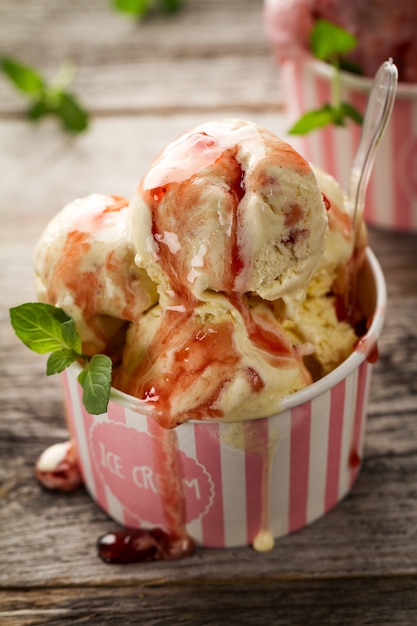 Leckere appetitliche Vanille Erdbeereis mit Marmelade und Minze in rosa Pappbecher auf Holztisch. Nahansicht.