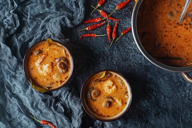 Leckere asiatische Suppe Tom Yam in kleinen Schalen mit Chili-Pfeffer-Garnelen-Pilzen, Kokosnuss und Limette auf dunklem Hintergrund