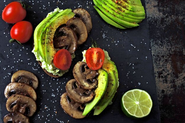 Leckere Avocado-Toasts mit Pilzen und Kirschtomaten, serviert auf einem Steinbrett.