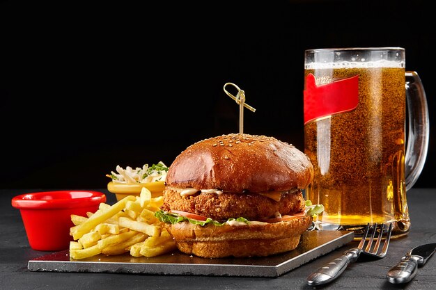 Leckere Burger Pommes Frites mit Sauce und Glas Bier auf schwarzem Brett