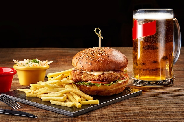 Leckere Burger Pommes Frites mit Sauce und Glas Bier auf schwarzem Brett