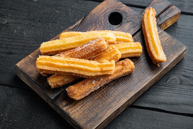 Leckere Churros mit Schokoladenkaramellsauce auf schwarzem Holztischhintergrund