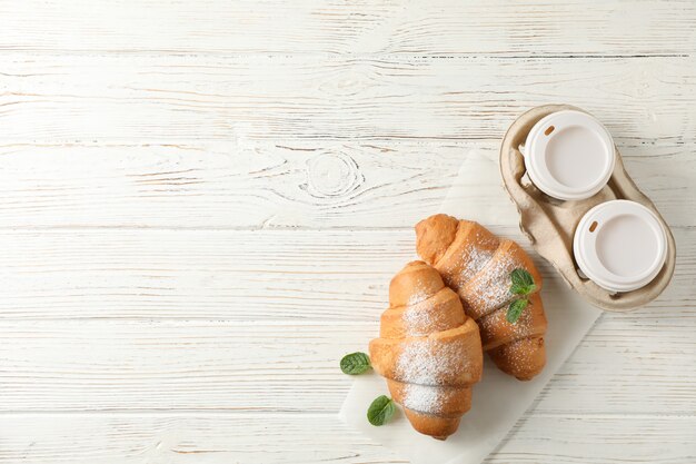 Leckere Croissants und Tassen mit Kaffee auf hölzernem Hintergrund, Draufsicht