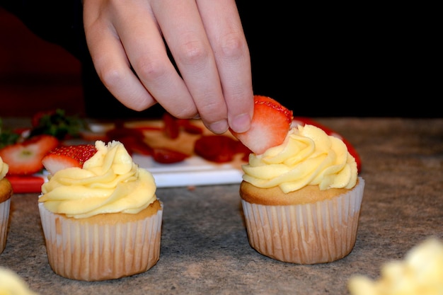 Leckere Cupcakes mit Buttercreme Person, die Cupcake mit Erdbeere dekoriert