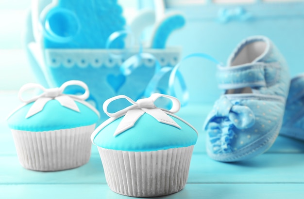 Leckere Cupcakes mit Schleife und Babyschuhen, dekorativer Kinderwagen und Fotoalbum auf farbiger Oberfläche