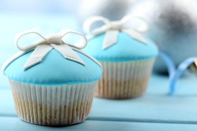 Leckere Cupcakes mit Schleife und Weihnachtsspielzeug auf farbiger Holzoberfläche