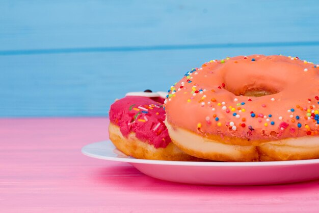 Leckere Donuts auf farbigem Hintergrund. Teller mit leckeren Kuchen auf Holztisch. Idee zum Frühstück.